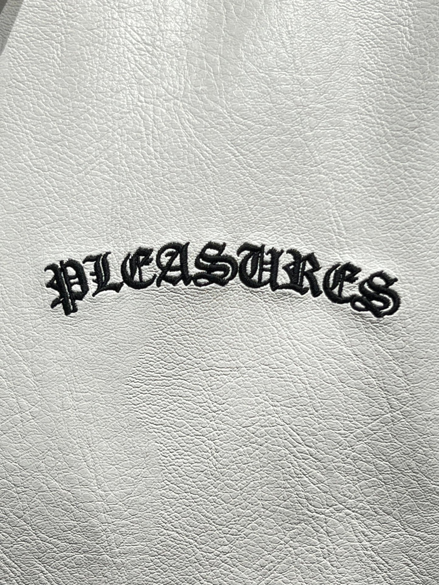A white Polyurethane bag with the word PLEASURES embroidered on it.