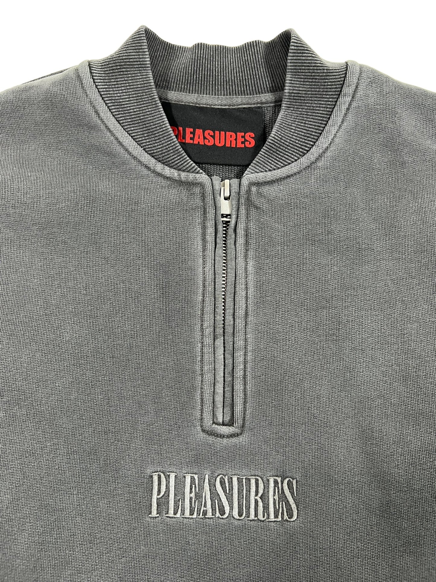 A grey cotton sweatshirt with the embroidered logo "PLEASURES" on it.