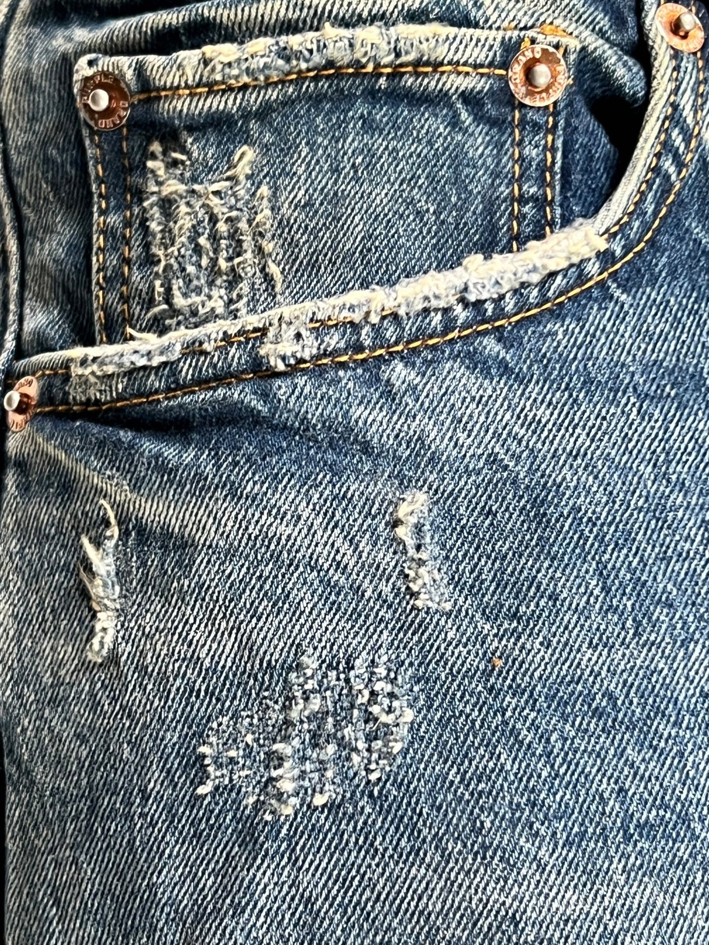 A pair of Purple Brand P001-THMI Thrashed Mid Indigo stretch denim jeans with holes in the pocket.