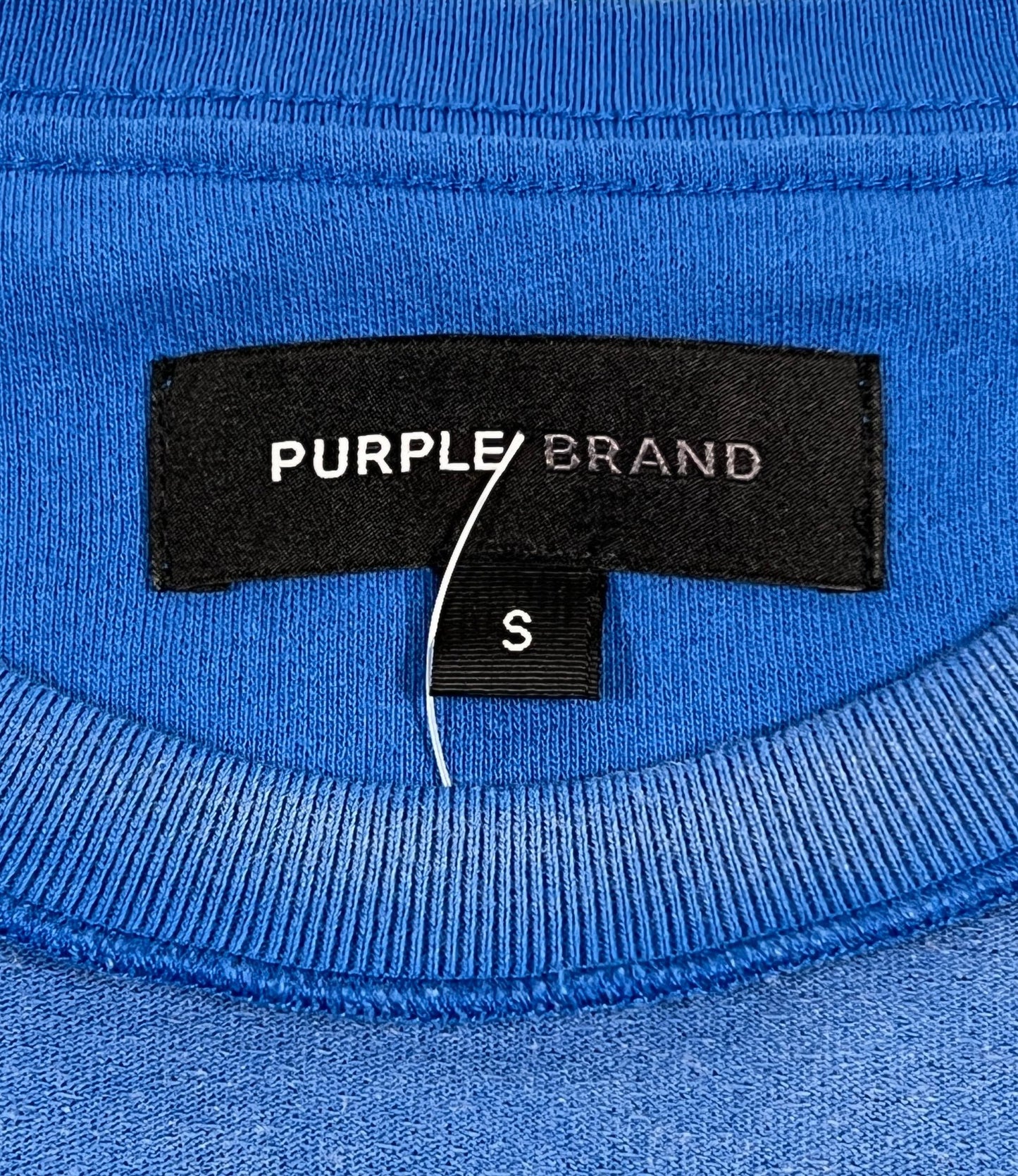 A close up of a PURPLE BRAND logo on a PURPLE BRAND P101-JUCB TEXTURED INSIDE OUT TEE BLUE.