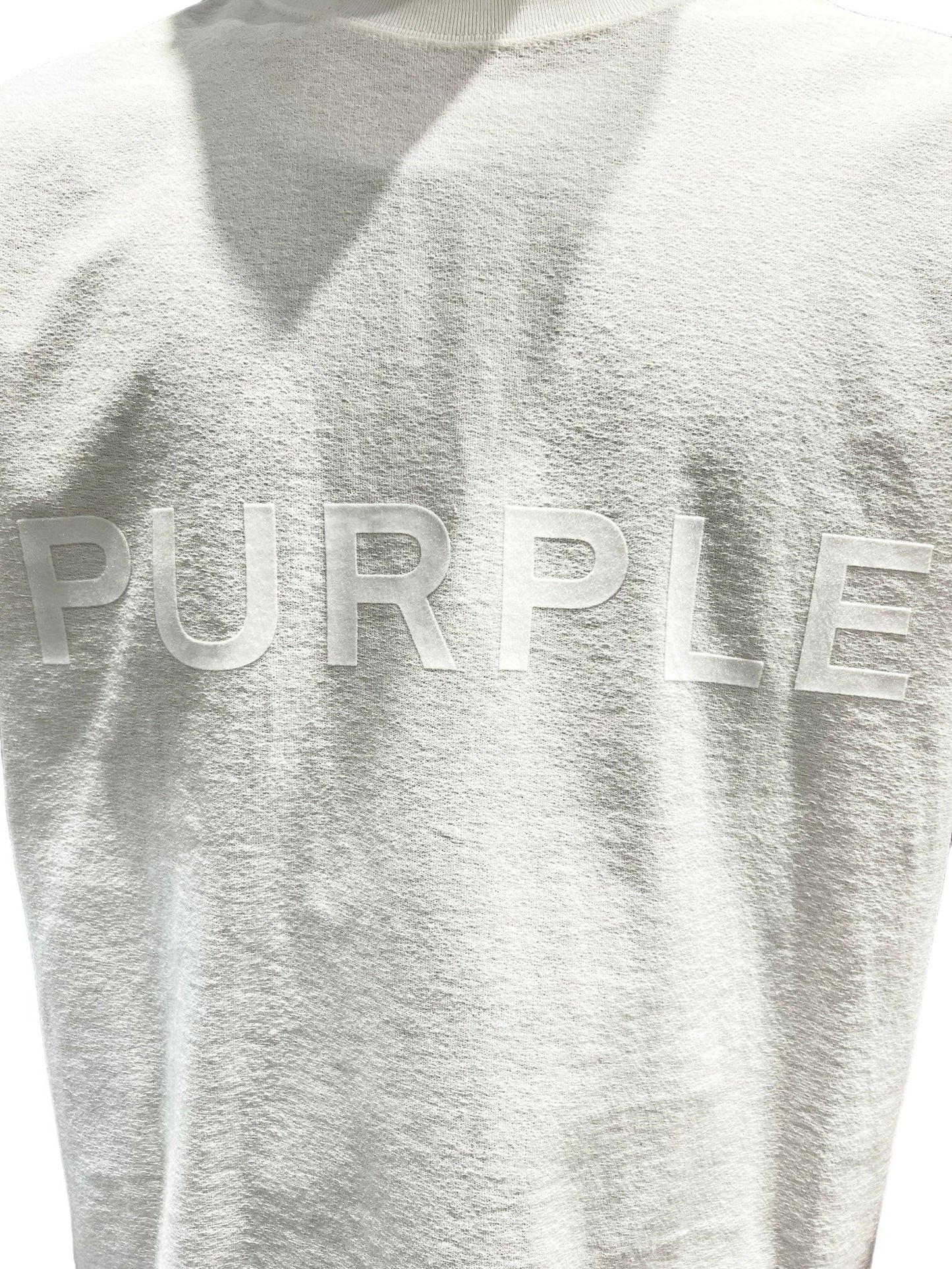 The back of an off-white PURPLE BRAND P104-JWCM TEXTURED JERSEY SS TEE with the word "PURPLE BRAND" on it.