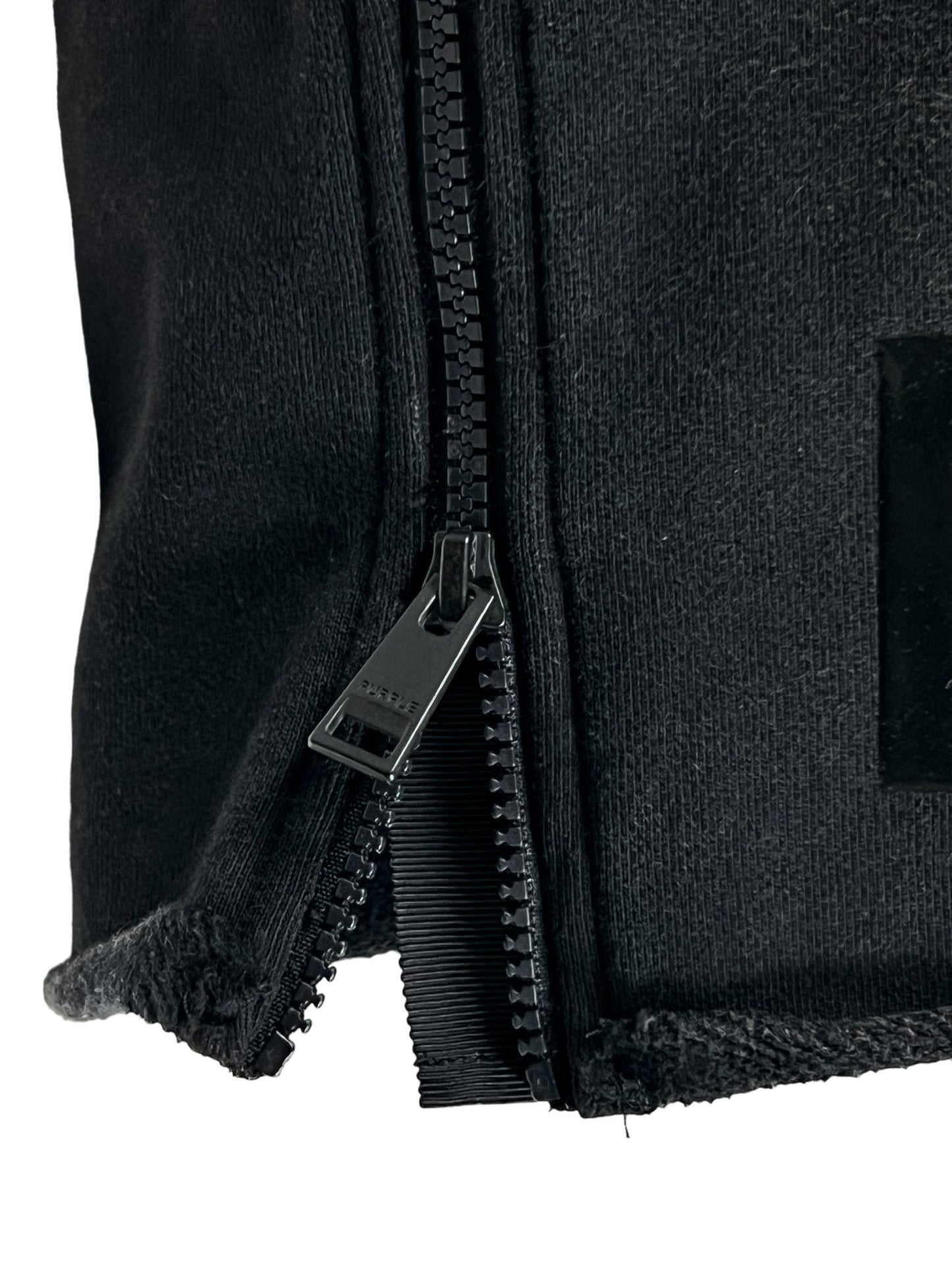 Close-up view of a partially unzipped black zipper on a black fabric. The bottom zipper edge shows frayed material, typical of well-worn PURPLE BRAND P479-MFBW MWT FLEECE SWEATSHORT BLACK from PURPLE BRAND.