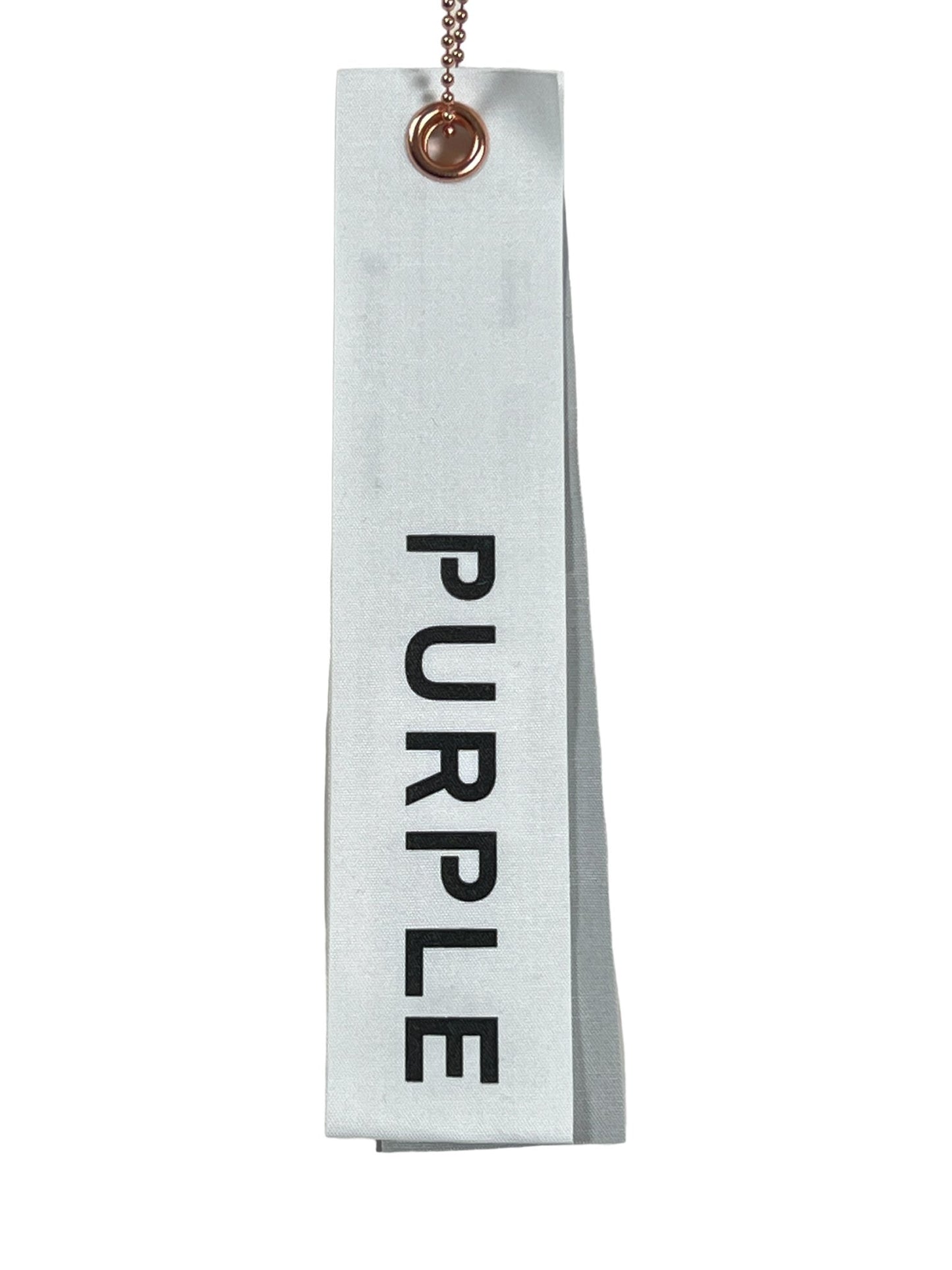 A light gray fabric swatch labeled "PURPLE" in black text, attached to a chain through a metal grommet, reminiscent of the quality found in PURPLE BRAND P479-MFBW MWT FLEECE SWEATSHORT BLACK by PURPLE BRAND.
