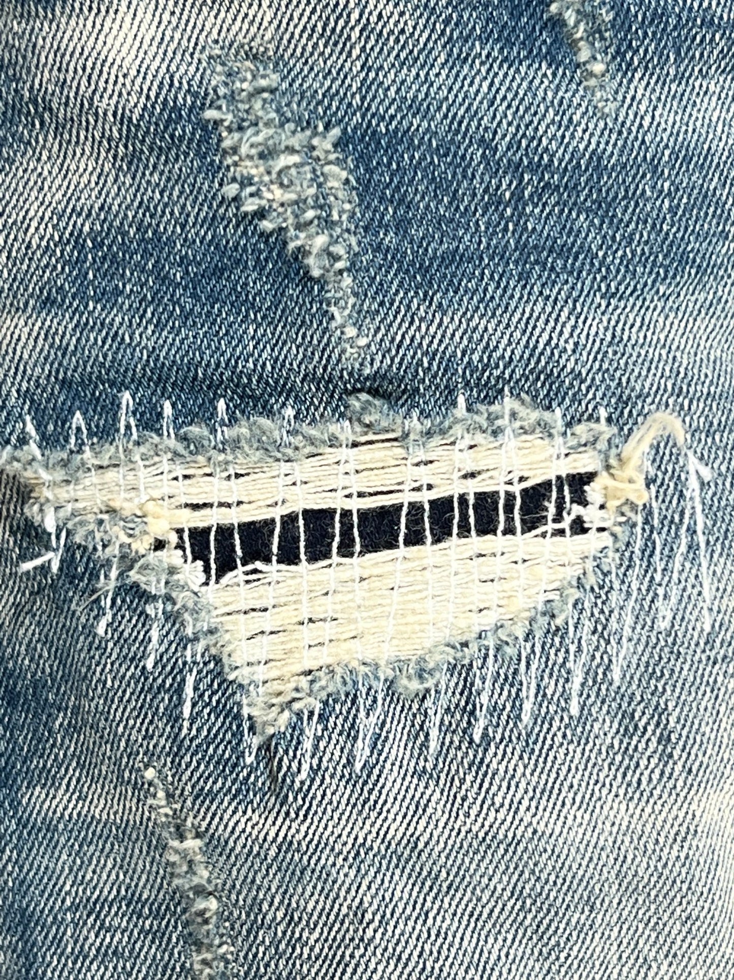 A close-up of a pair of PURPLE BRAND jeans, style P001-MIVM MID INDIGO VINTAGE MARBLE BLEACH, with holes in them.