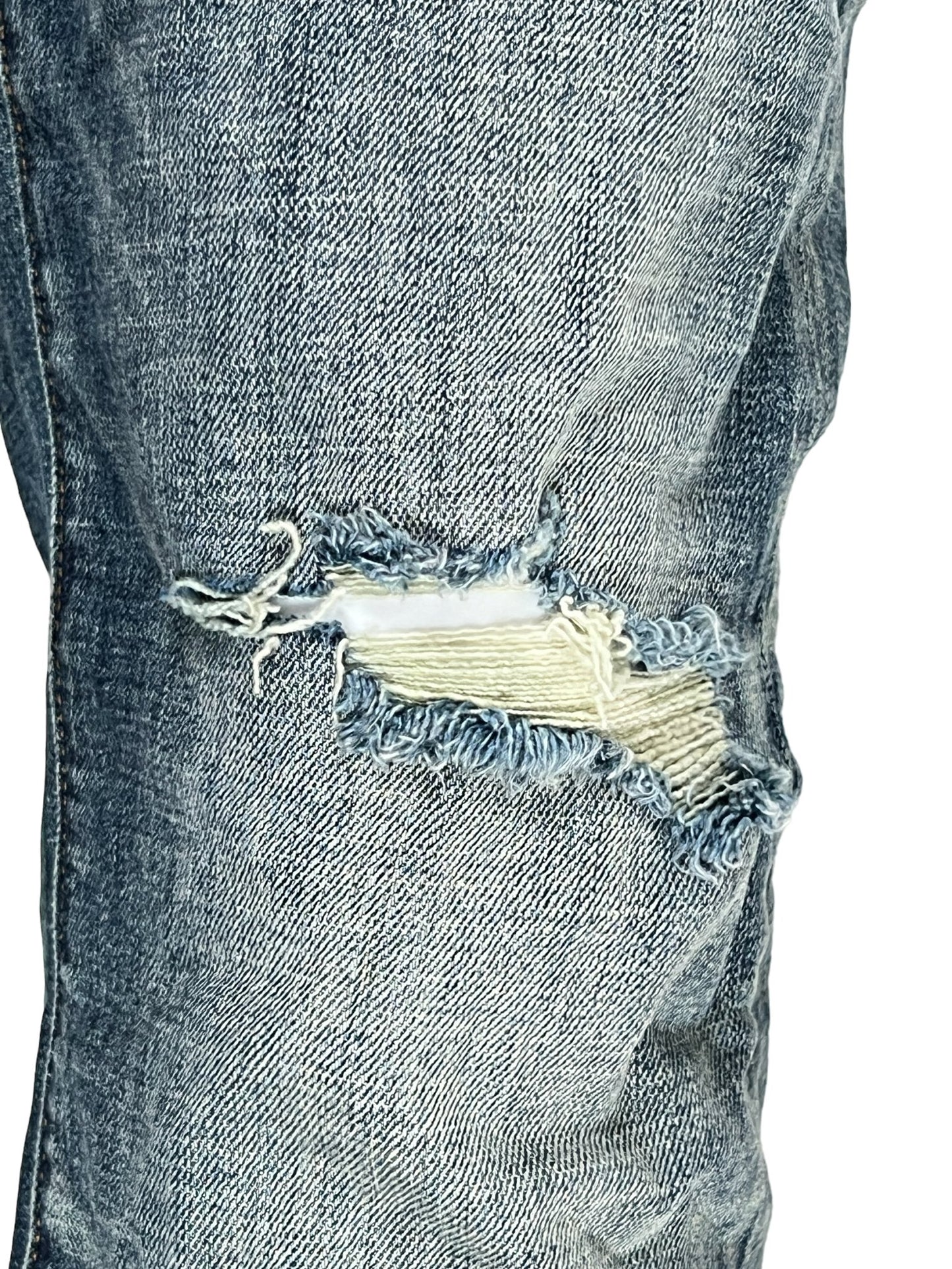 A close-up of a pair of torn PURPLE BRAND jeans with a 1-year fade flare.