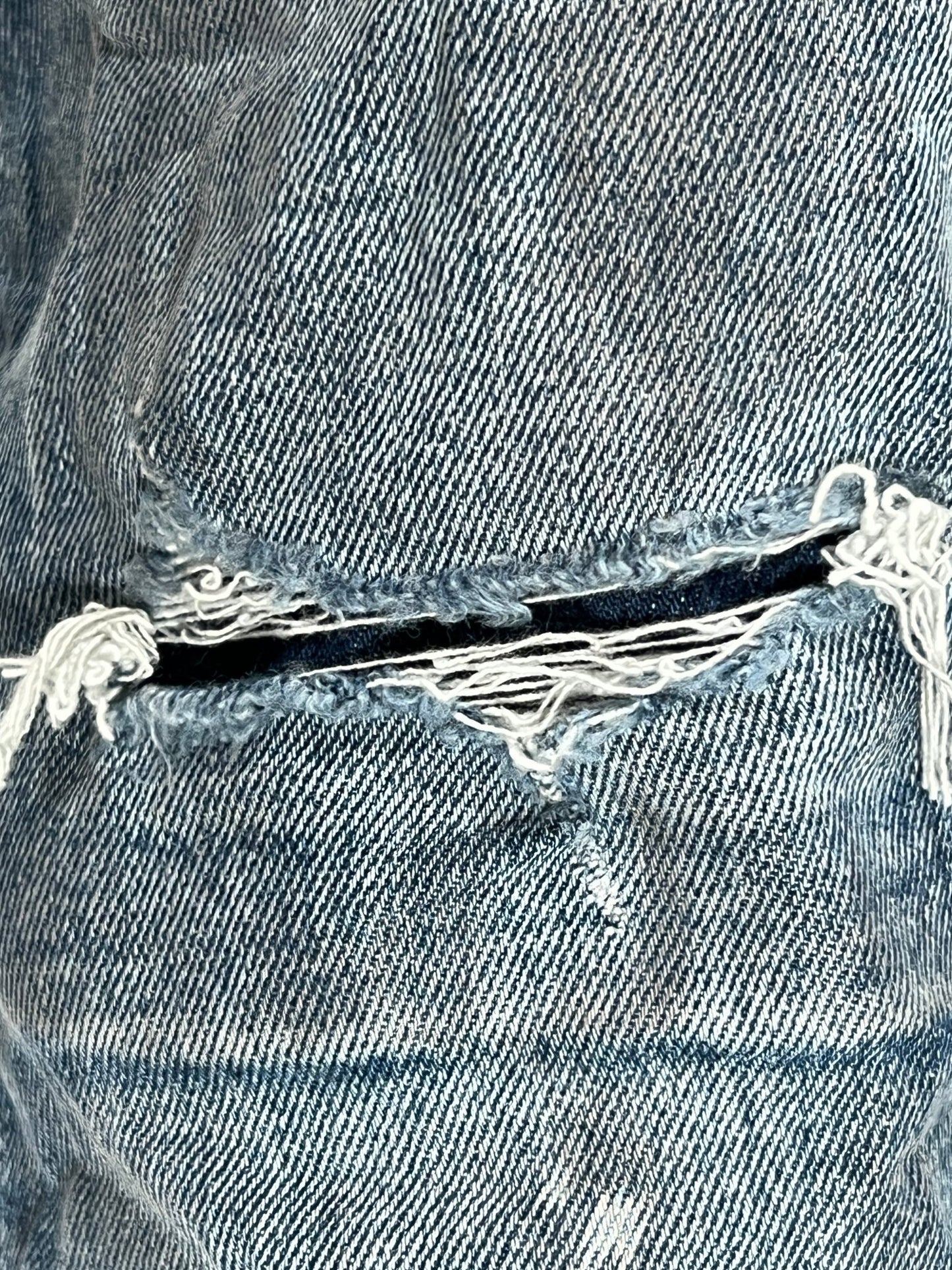 A pair of PURPLE BRAND vintage blue jeans with a hole in the pocket.