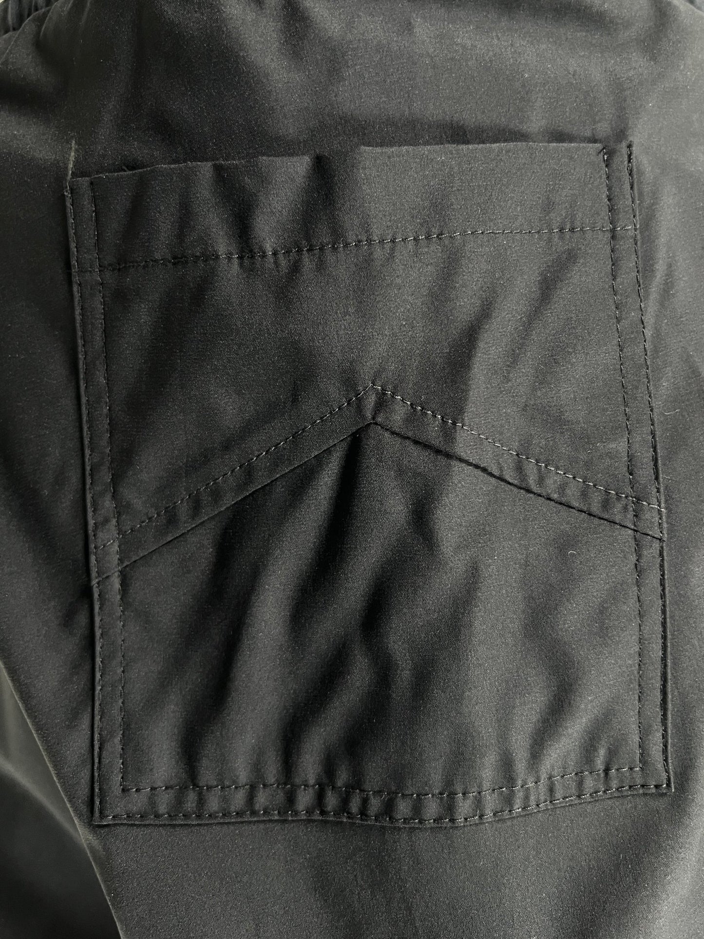 A black RHUDE Nylon Spandex swim trunks pocket with reinforced stitching on gray material.