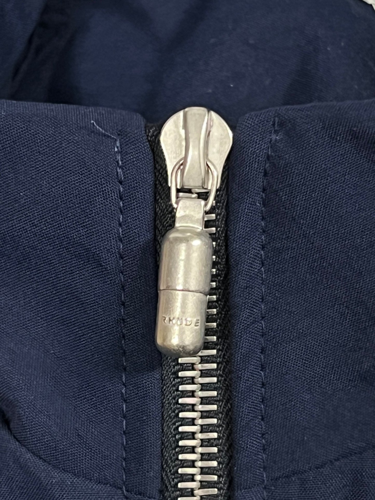 A close up of a zipper with custom RHUDE PALM hardware on a blue RHUDE PALM TRACK JACKET NAVY.