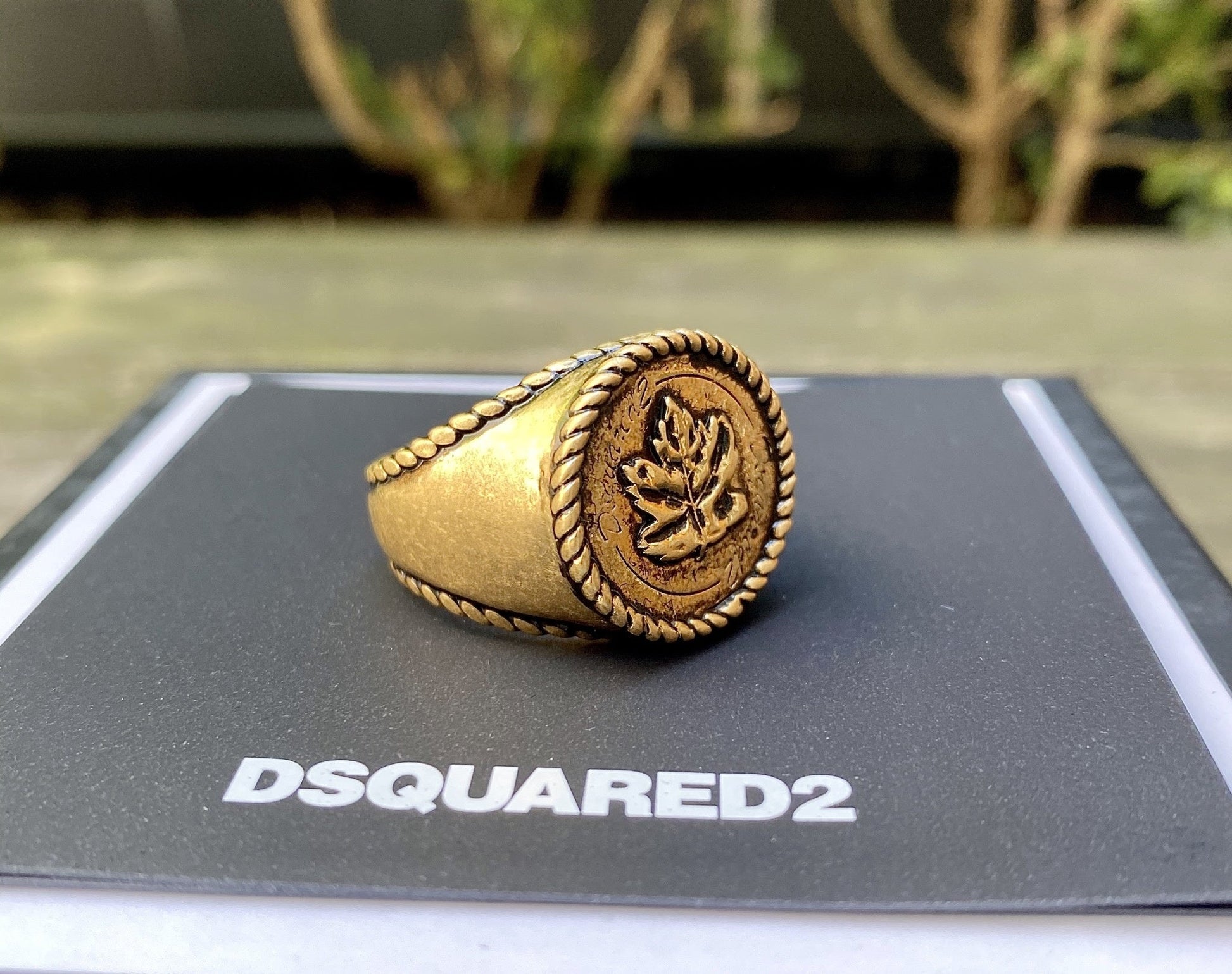 A metallic gold DSQUARED2 RIM0019 ring on top of a box.