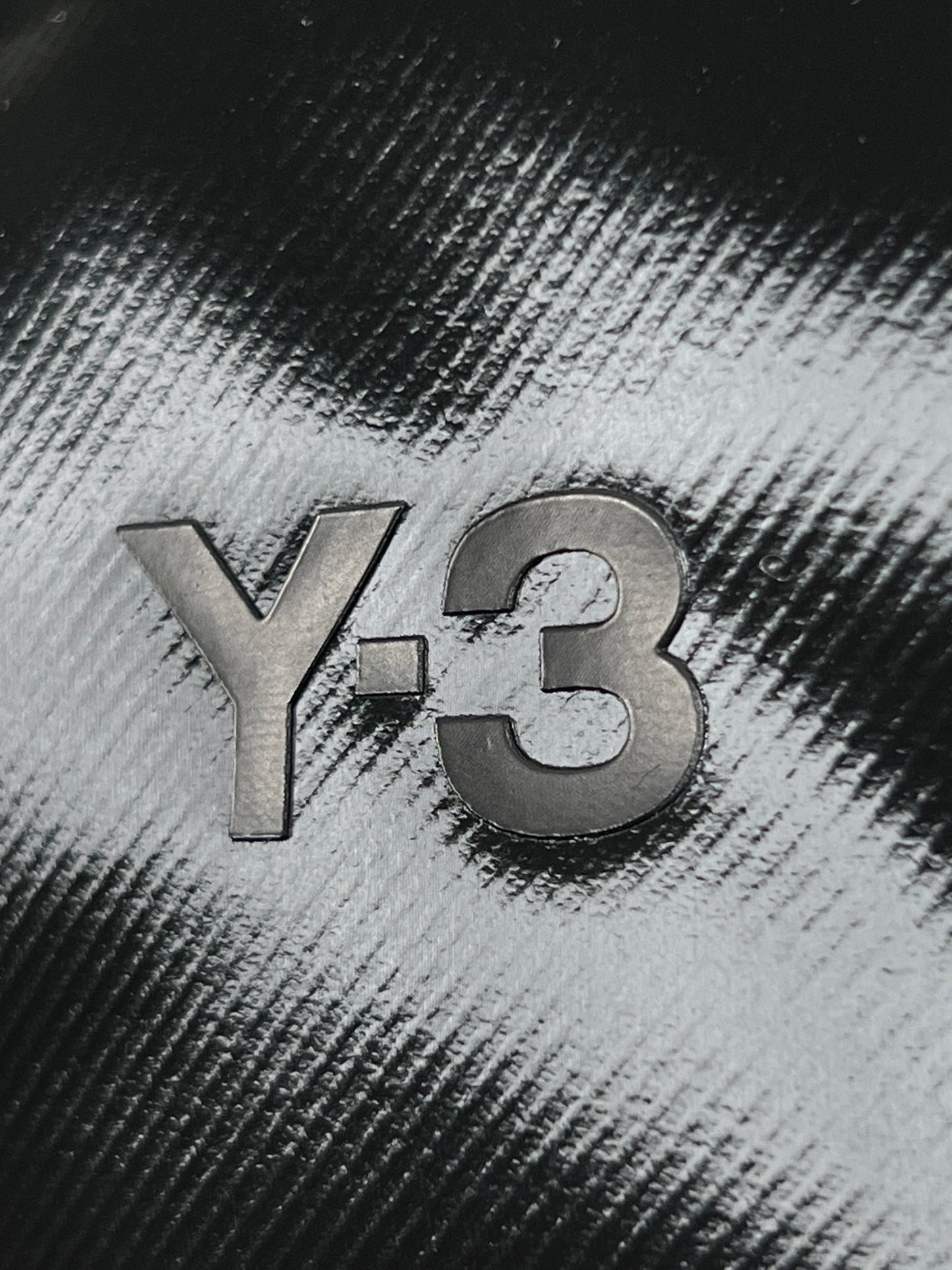 A close up of the ADIDAS x Y-3 IJ9901 Y-3 X BODY BAG BLACK logo on a black and white top with adjustable shoulder strap.